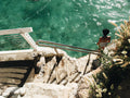 Person sitting on a ledge overlooking clear blue water