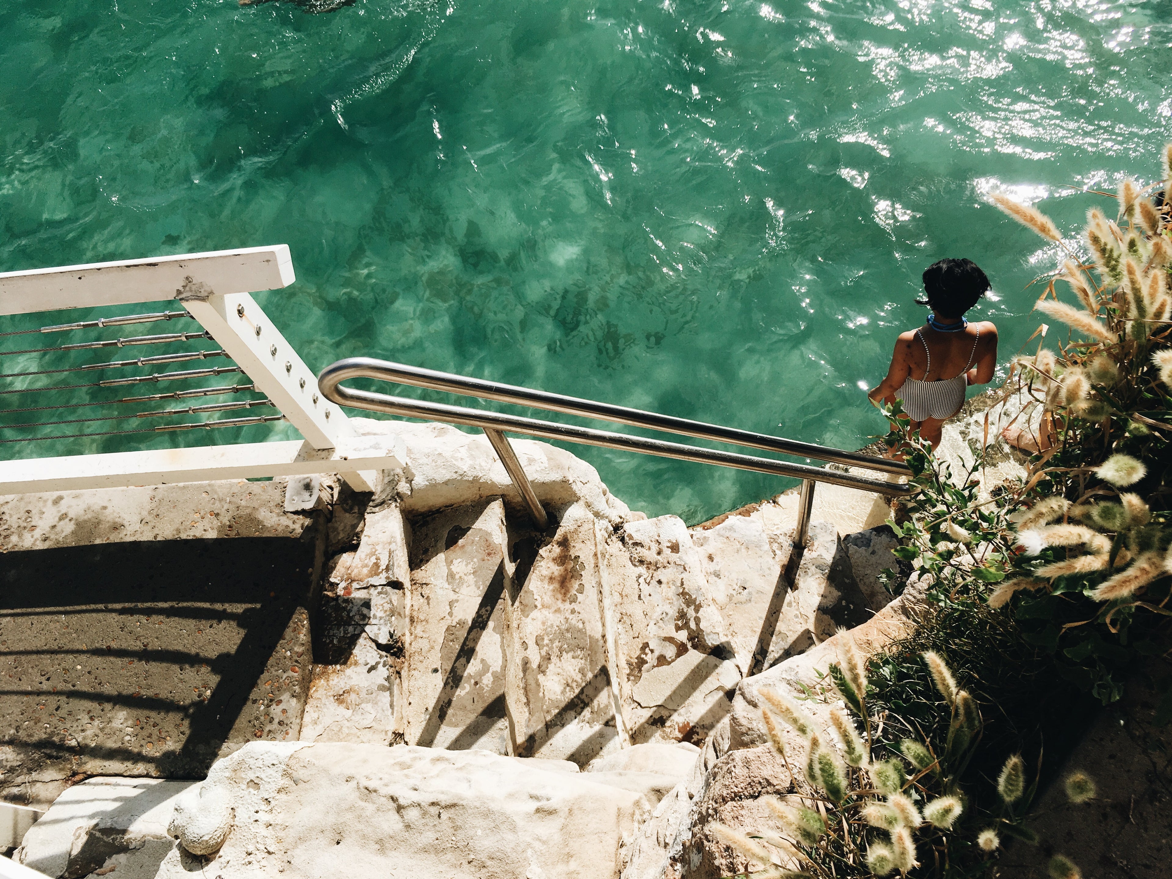 Person sitting on a ledge overlooking clear blue water