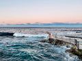 People enjoying a swim at a coastal pool with ocean waves and a dock.