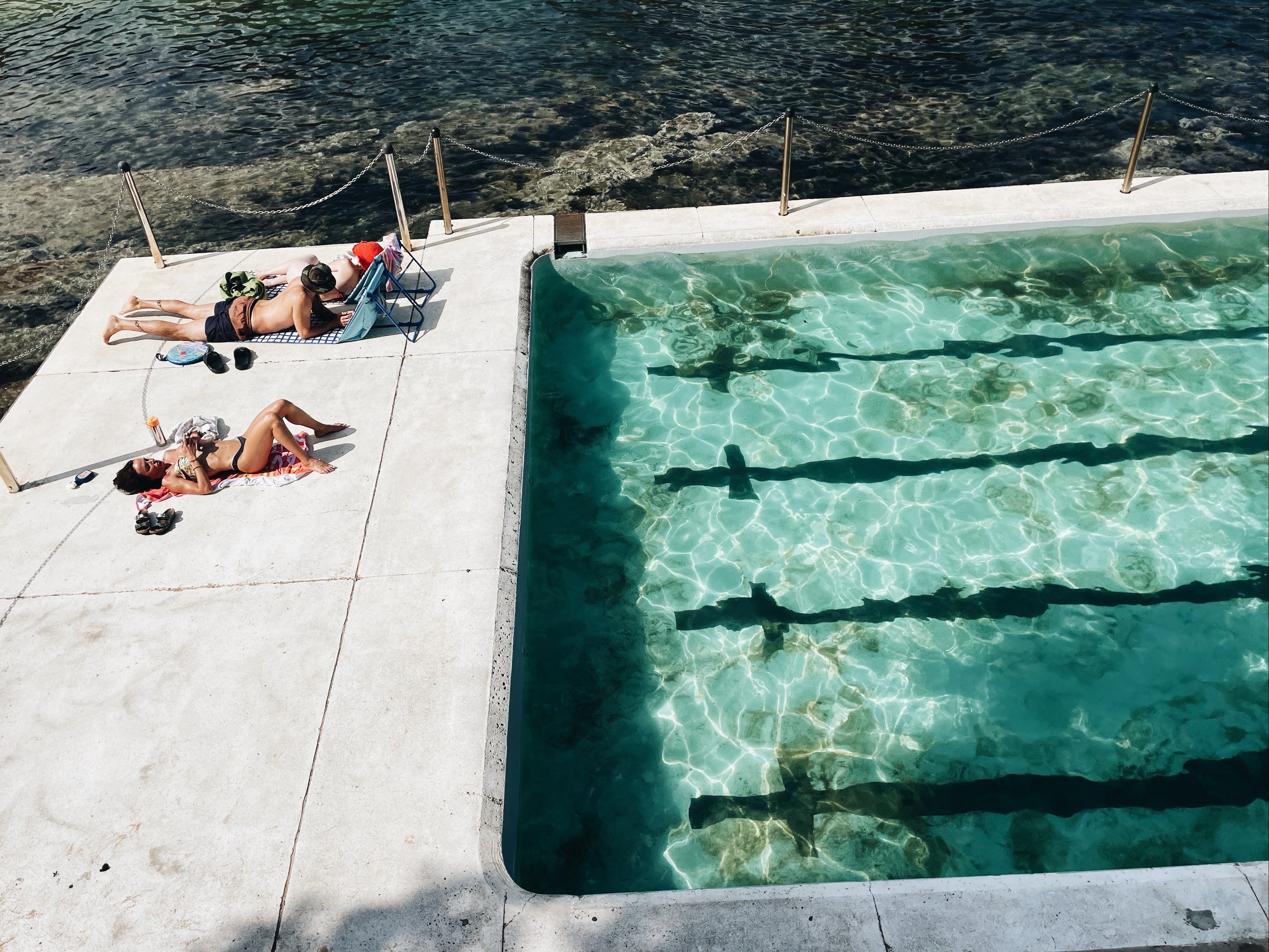 People sunbathing by a pool with clear water