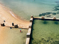 Beach scene with people near a concrete barrier and clear water.