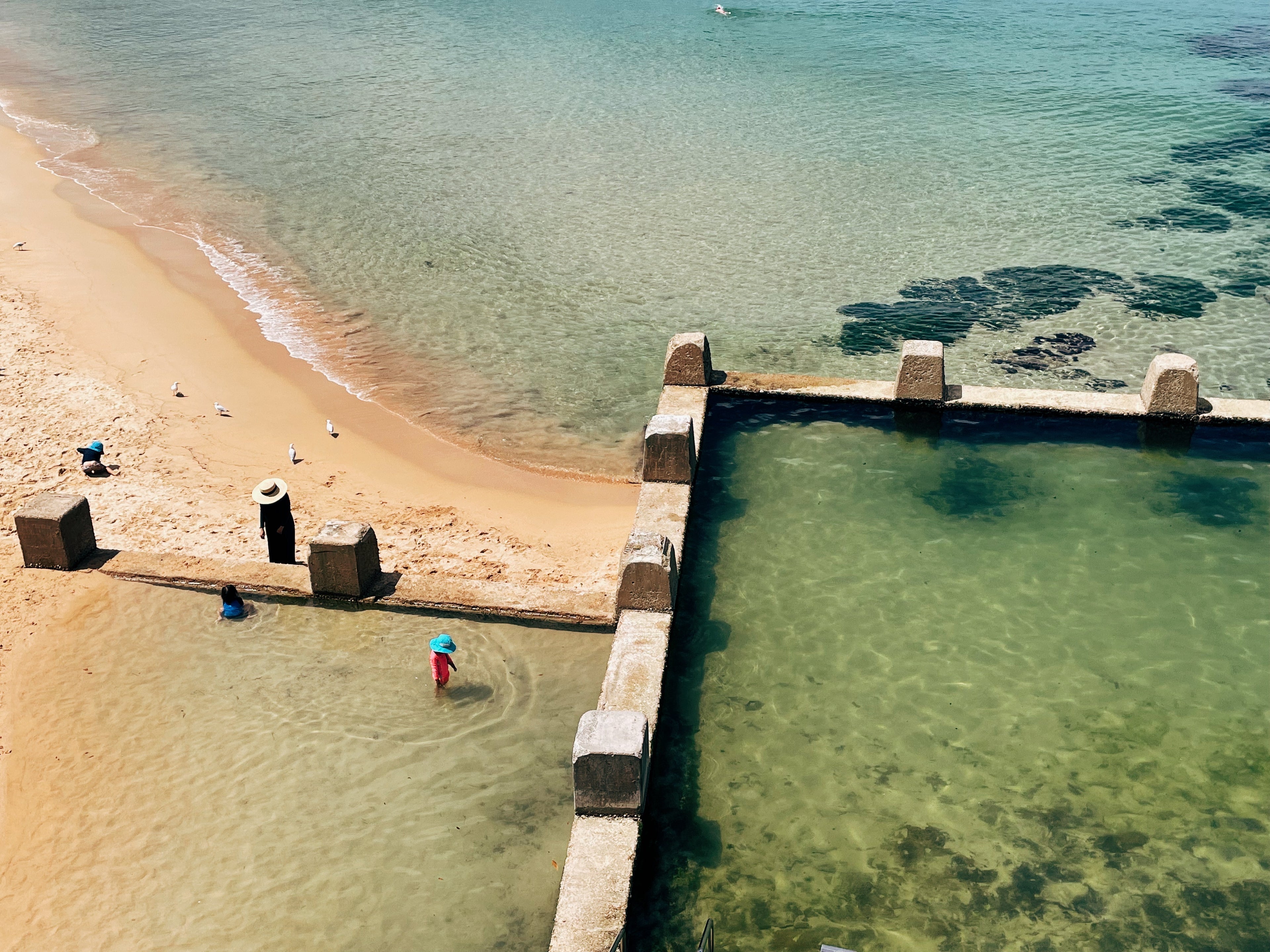 Beach scene with people near a concrete barrier and clear water.