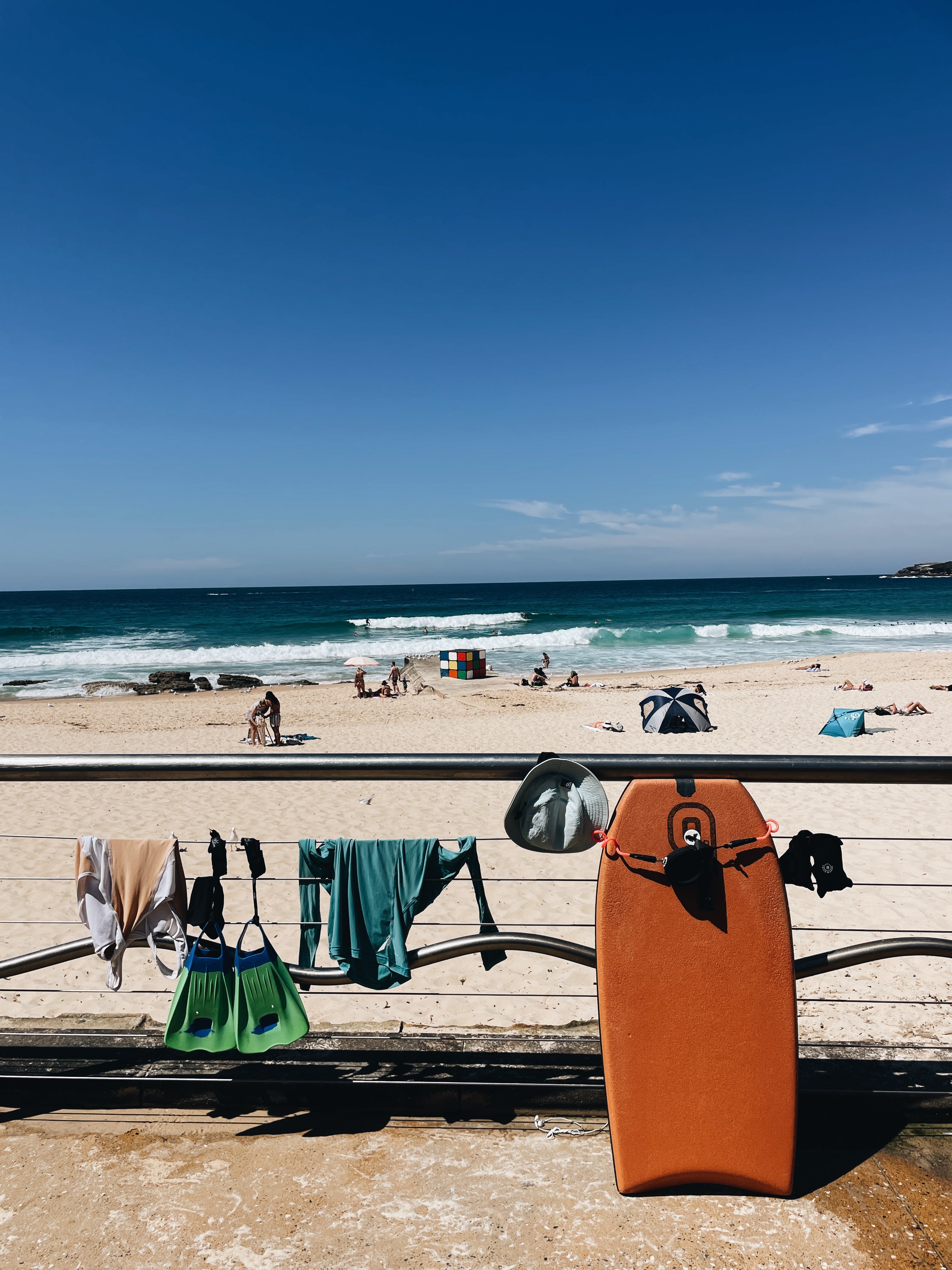 Beach scene with a drying rack with clothes and a bodyboard against a blue sky.