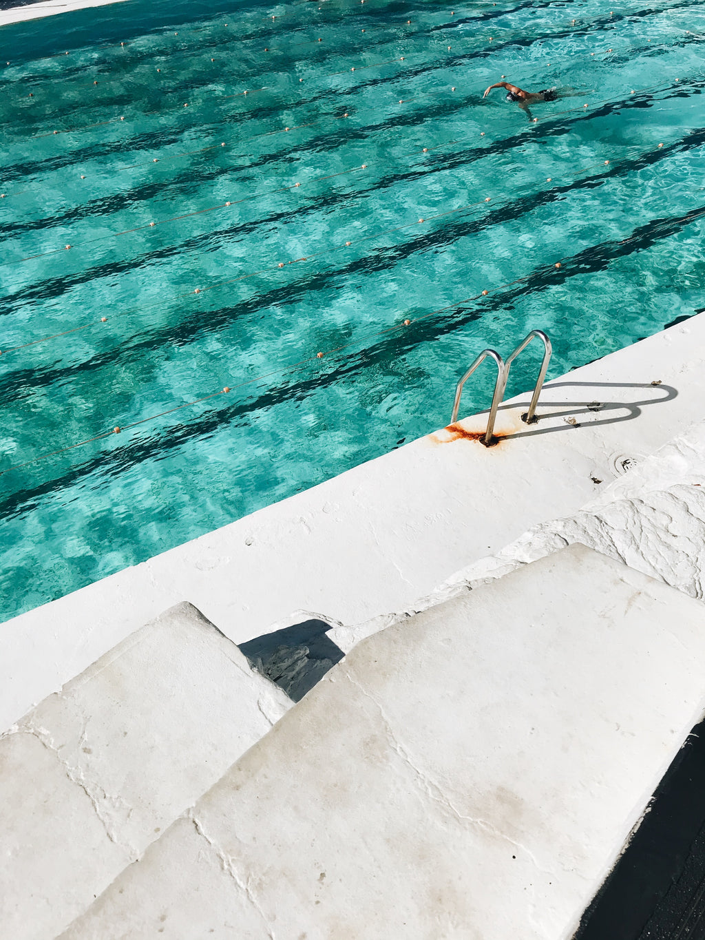 Person swimming in a pool with visible lane lines and a concrete edge.