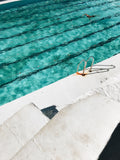 Person swimming in a pool with visible lane lines and a concrete edge.