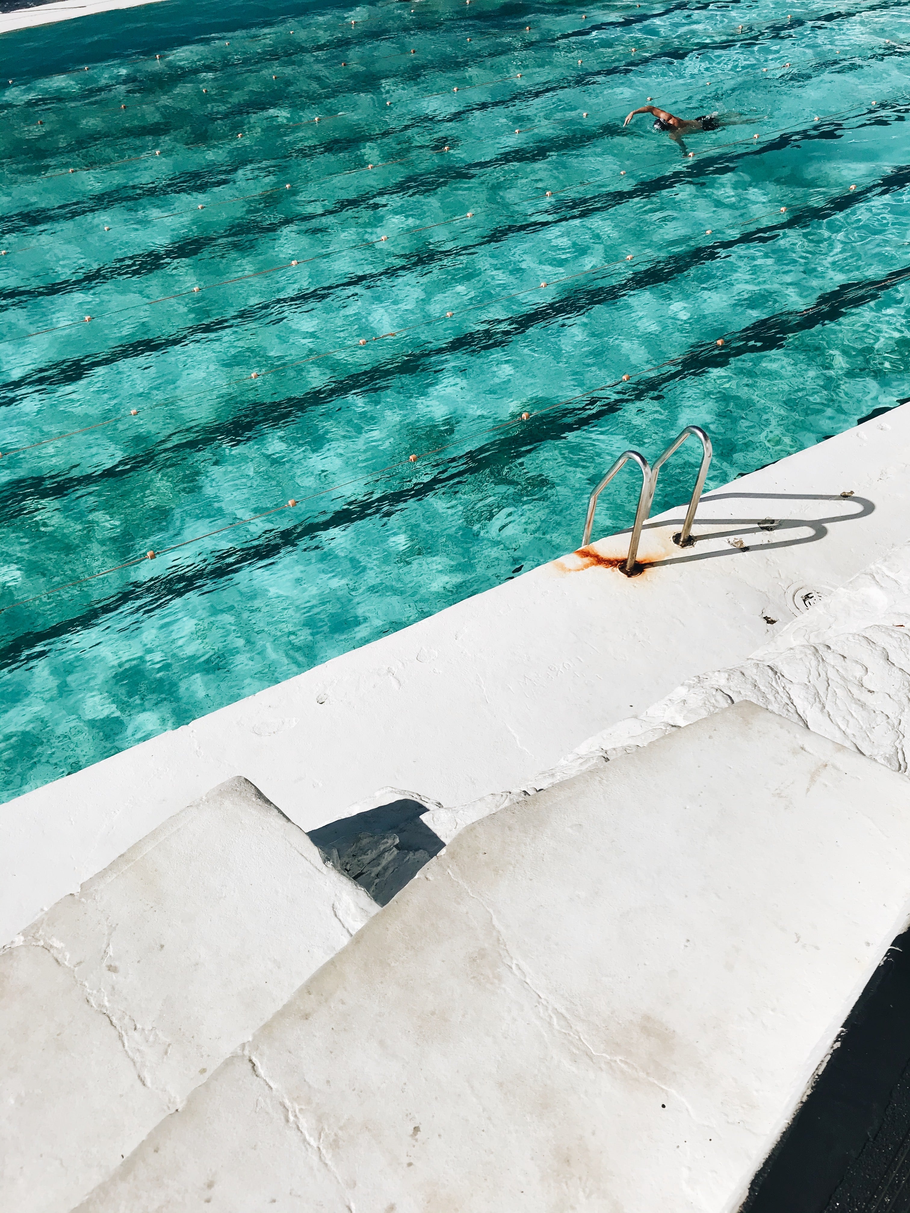 Person swimming in a pool with visible lane lines and a concrete edge.