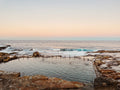 Natural rock pool by the ocean with people swimming at sunset.