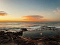 Sunset over a rocky beach with people in the water