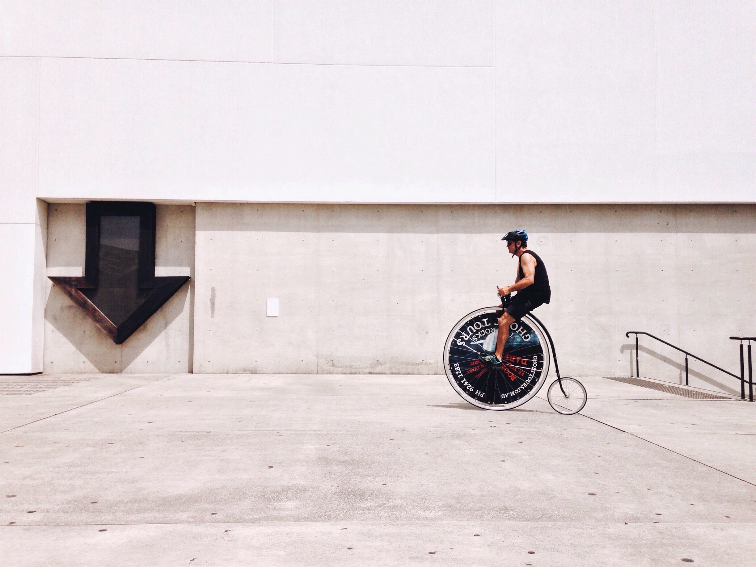 Person riding a unicycle with a large front wheel and small back wheel on a concrete surface.