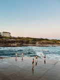 People swimming and playing in the ocean with a scenic view of cliffs and buildings.